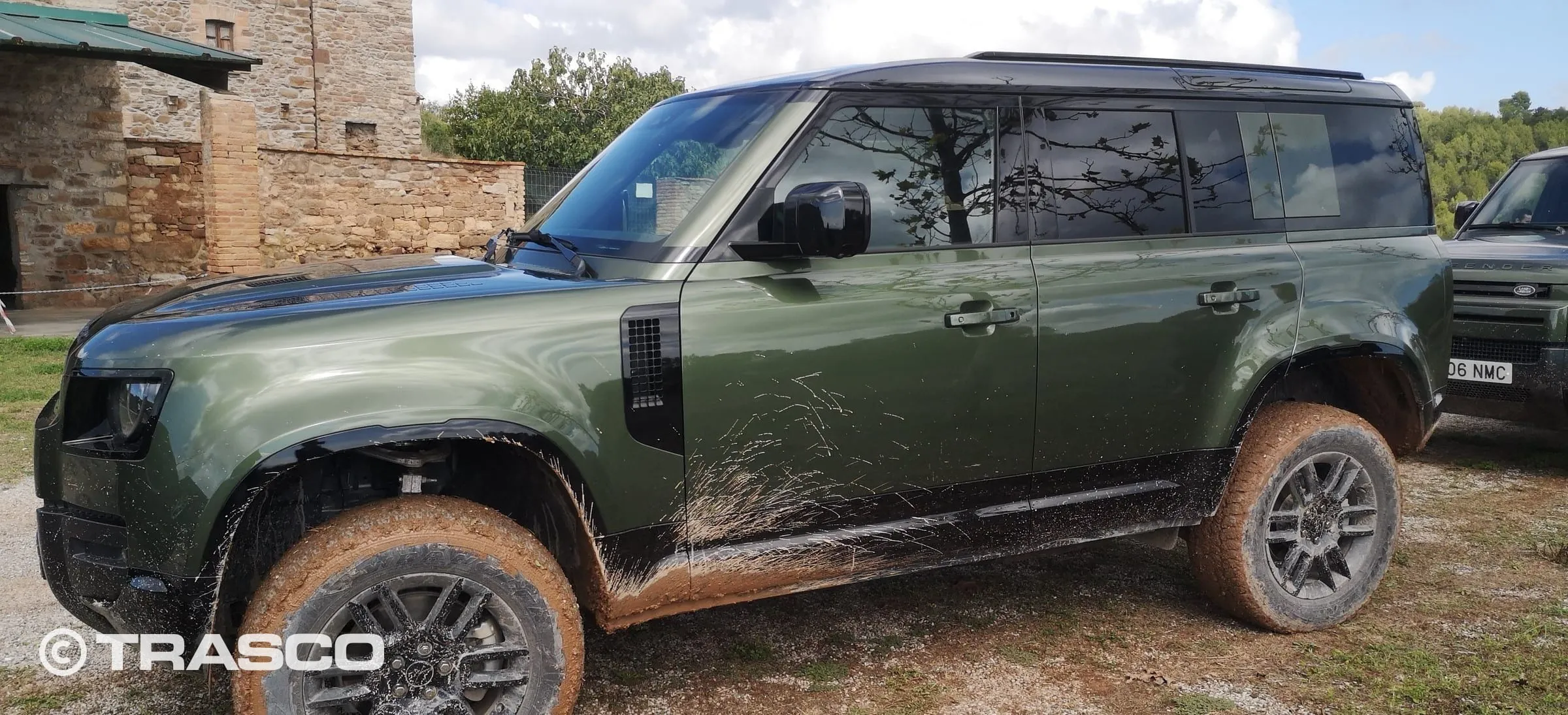 Defender avec de la boue sur les roues et les bas de caisse devant un bâtiment en pierre naturelle à Les Comes